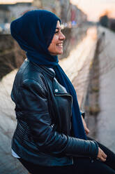 Happy young woman in hijab by city canal - CUF52848