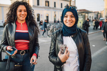 Junge Frau im Hidschab mit bester Freundin auf einer Straße in der Stadt - CUF52850