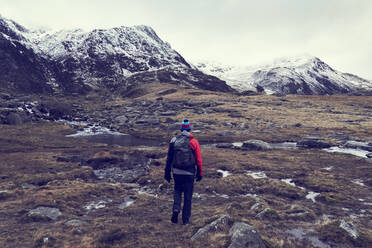 Männlicher Wanderer mit Blick auf eine zerklüftete Landschaft mit schneebedeckten Bergen, Rückansicht, Llanberis, Gwynedd, Wales - CUF52858