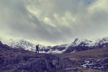 Männlicher Wanderer beim Wandern durch eine zerklüftete Landschaft mit schneebedeckten Bergen, Llanberis, Gwynedd, Wales - CUF52879