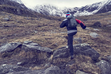 Männlicher Wanderer beim Aufstieg durch zerklüftete Landschaft mit schneebedeckten Bergen, Rückansicht, Llanberis, Gwynedd, Wales - CUF52881