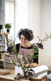 Lächelnde junge Frau mit Laptop in einem kleinen Laden mit Pflanzen - HAPF03017