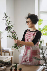 Lächelnde junge Frau arrangiert Blumen in einem kleinen Laden - HAPF03024