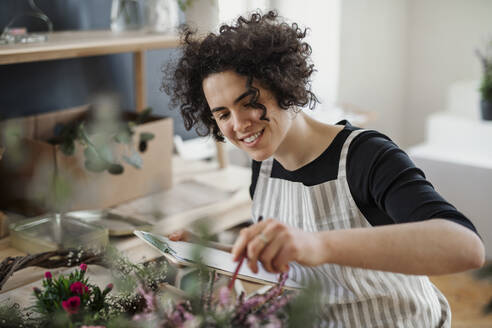 Lächelnde junge Frau mit Klemmbrett in einem kleinen Laden mit Pflanzen - HAPF03032