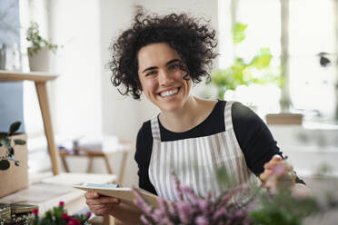 Porträt einer glücklichen jungen Frau mit Klemmbrett in einem kleinen Laden mit Pflanzen - HAPF03033