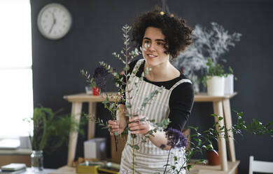 Smiling young woman arranging flowers in a small shop - HAPF03043