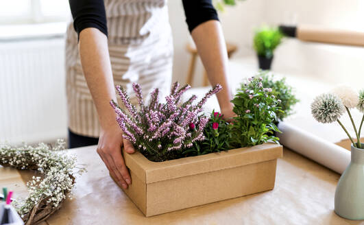 Close-up of woman with flowers inside a cardboard box on table - HAPF03054