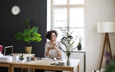 Smiling young woman sitting at table looking sideways - HAPF03059