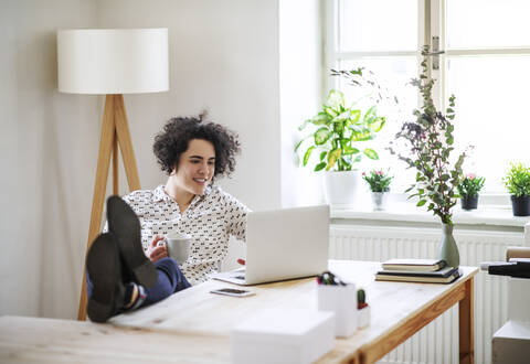 Entspannte junge Frau arbeitet am Laptop am Schreibtisch, lizenzfreies Stockfoto