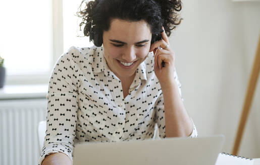 Lächelnde junge Frau mit Headset und Laptop bei der Arbeit am Schreibtisch - HAPF03066