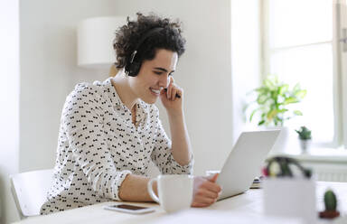 Smiling young woman with headset and laptop working at desk - HAPF03067