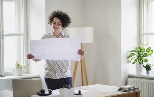 Smiling young woman studying a plan in office - HAPF03071