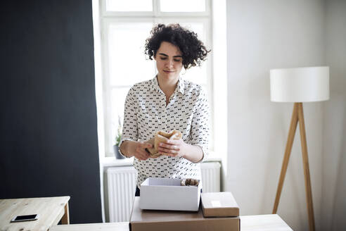 Young woman wrapping a product at table - HAPF03074