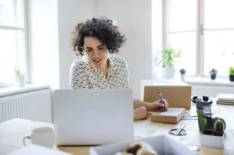 Smiling young woman preparing a package at desk stock photo