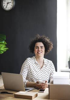 Portrait of smiling young woman sitting at desk in office - HAPF03082