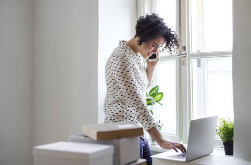 Lächelnde junge Frau am Telefon mit Laptop im Home Office - HAPF03087