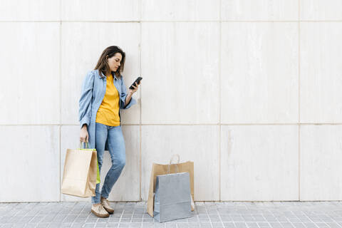 Junge brünette Frau benutzt Smartphone nach dem Einkaufen, lizenzfreies Stockfoto