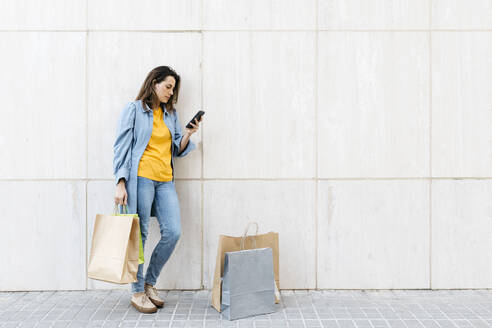 Junge brünette Frau benutzt Smartphone nach dem Einkaufen - JRFF03794