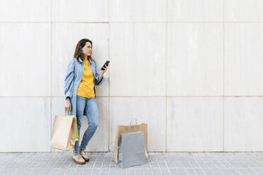 Young brunette woman using smartphone after shopping - JRFF03795