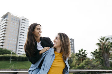 Laughing woman carrying her best friend piggyback in a park - JRFF03802