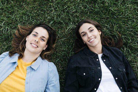 Porträt von zwei Freunden, die in die Kamera schauen, im Gras liegend, lizenzfreies Stockfoto