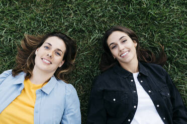 Portrait of two friends looking at camera, lying on the grass - JRFF03808