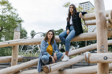 Two friends on playground, sitting on jungle gym - JRFF03814