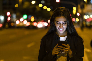 Junge Frau benutzt Smartphone in der nächtlichen Stadt - JRFF03821