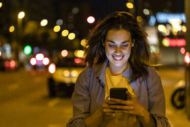 Junge Frau benutzt Smartphone in der nächtlichen Stadt - JRFF03822