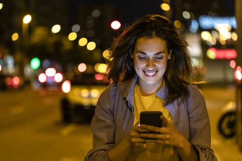 Junge Frau benutzt Smartphone in der nächtlichen Stadt - JRFF03822