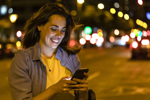 Junge Frau benutzt Smartphone in der nächtlichen Stadt - JRFF03823
