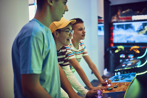 Teenage friends playing with a gaming machine in an amusement arcade - ZEDF02673