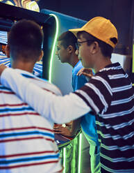 Junge, der seine Freunde beim Spielen mit einem Spielautomaten in einer Spielhalle beobachtet - ZEDF02675