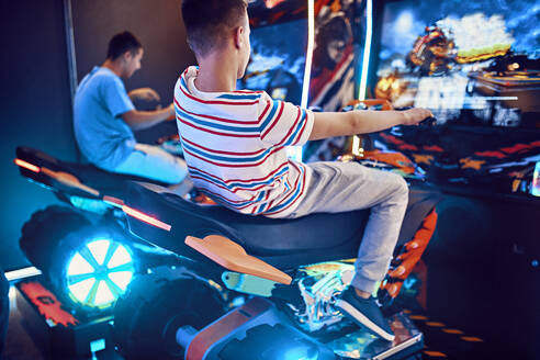 Teenage friends playing with a driving simulator in an amusement arcade - ZEDF02676