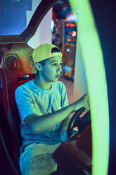 Teenage boy playing with a driving simulator in an amusement arcade - ZEDF02686