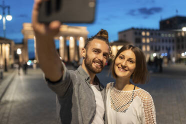 Happy couple taking a selfie at Brandenburg gate at blue hour, Berlin, Germany - WPEF02134