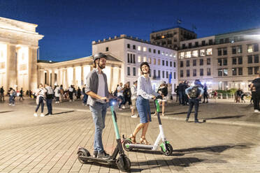 Junges Paar mit Elektrorollern am Brandenburger Tor bei Nacht, Berlin, Deutschland - WPEF02143