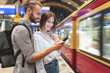 Junges Paar, das am Bahnhof auf den Zug wartet und ein Smartphone benutzt, Berlin, Deutschland - WPEF02158