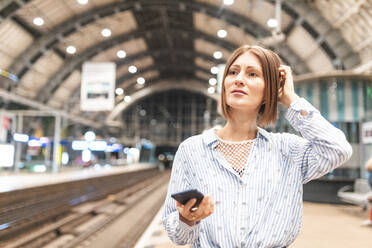 Junge unglückliche Frau, die auf dem Bahnhof ihr Smartphone benutzt - WPEF02160