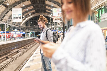 Menschen, die am Bahnhof auf den Zug warten und Smartphones benutzen, Berlin, Deutschland - WPEF02161