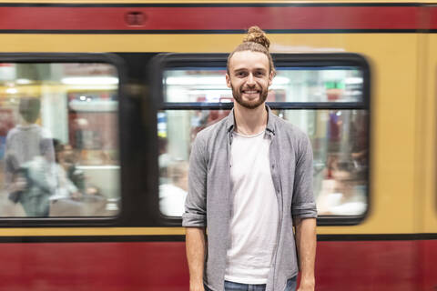 Junger Mann am Bahnhof mit unscharfem Zug als Hintergrund, lizenzfreies Stockfoto