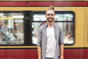 Junger Mann am Bahnhof mit unscharfem Zug als Hintergrund - WPEF02163