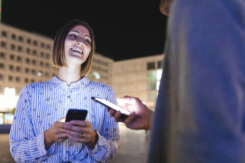 Glückliches Paar in der Stadt bei Nacht, das seine Telefone überprüft, Berlin, Deutschland, lizenzfreies Stockfoto