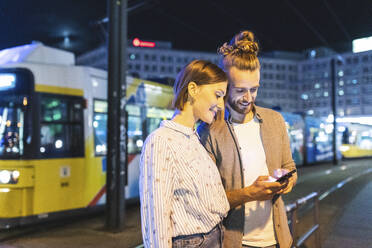 Glückliches Paar in der Stadt bei Nacht, das seine Telefone überprüft, Berlin, Gernany - WPEF02171