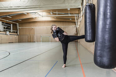 Female kickboxer practising at punchbag in sports hall - STBF00461