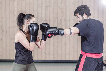 Female boxer sparring with coach in sports hall - STBF00479