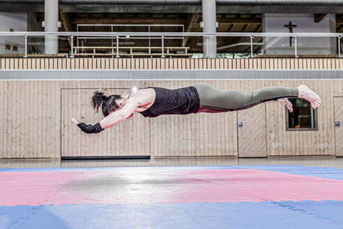 Frau, die in einer Sporthalle trainiert und in der Luft schwebt - STBF00483