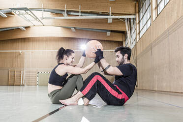 Mann und Frau beim Üben mit einem Medizinball in einer Sporthalle - STBF00487