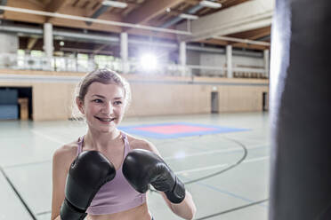 Lächelnde Boxerin beim Training am Boxsack in der Sporthalle - STBF00489