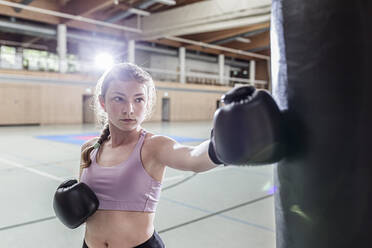 Female boxer practising at punchbag in sports hall - STBF00490